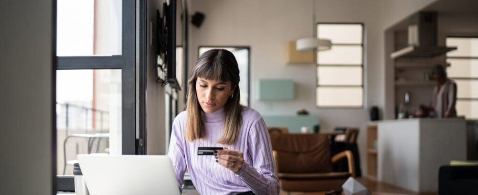 Young-woman-holding-credit-card-while-using-laptop-at-home_FG-Trade.jpg